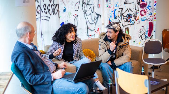 three people sitting together on a couch talking with graffiti in the background