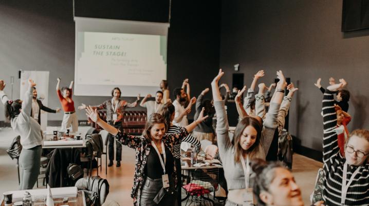 Attendees of a training programme holding their arms up in a room, probably following instructions by the trainer