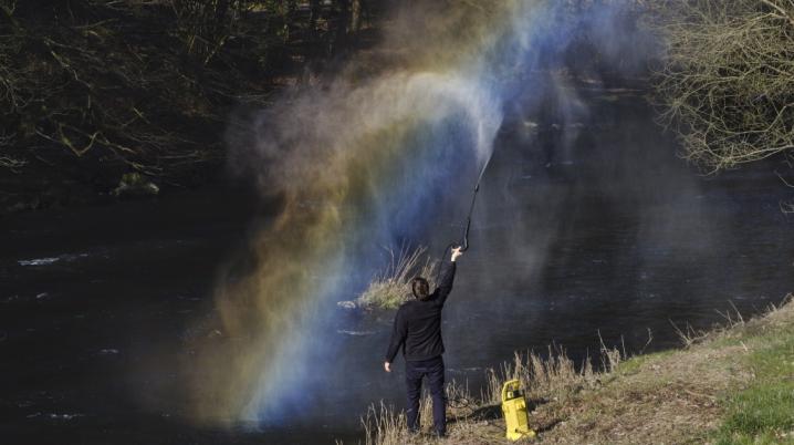 Picture of a person spraying water above a river in the Black Forest, resulting in a rainbow