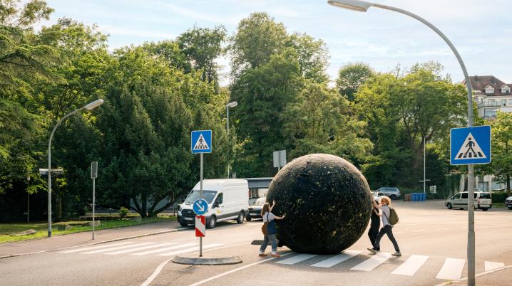 Three people rolling a giant black ball through a street