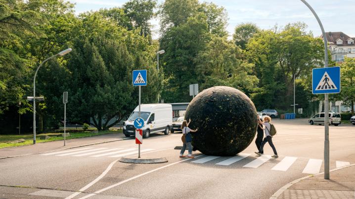 Three people rolling a giant black ball through a street