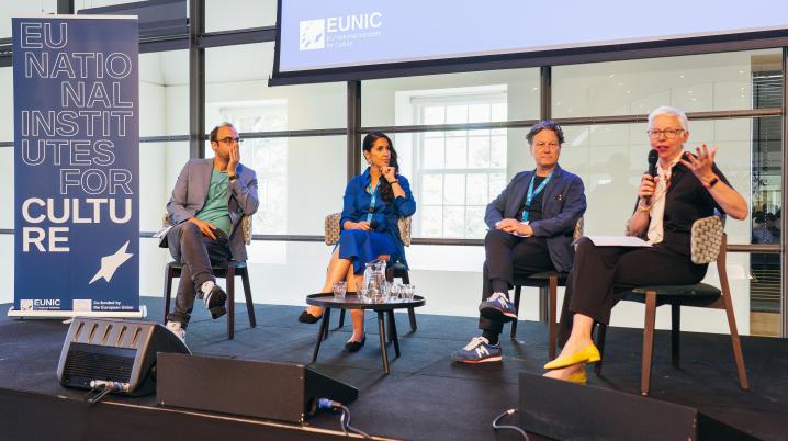 four people sitting on a stage for a panel talk, a woman is taljing in the microphone to an invisible audience