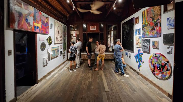 a group of people in an exhibition space watching colourful artworks on the wall