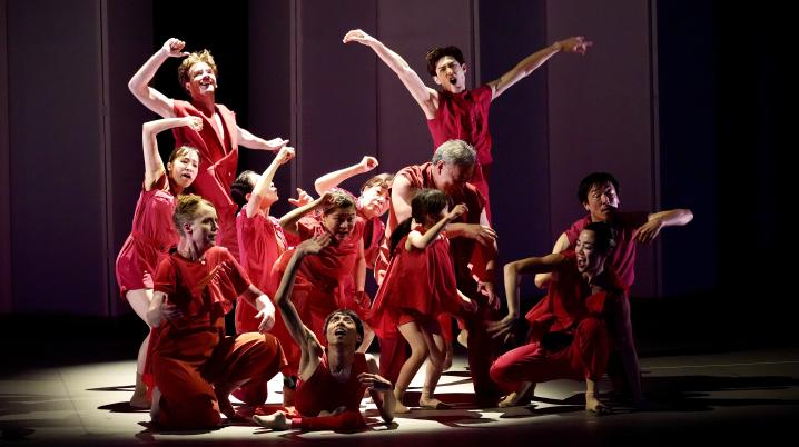 a large group of dancers all dressed in red in the spotlights on a stage