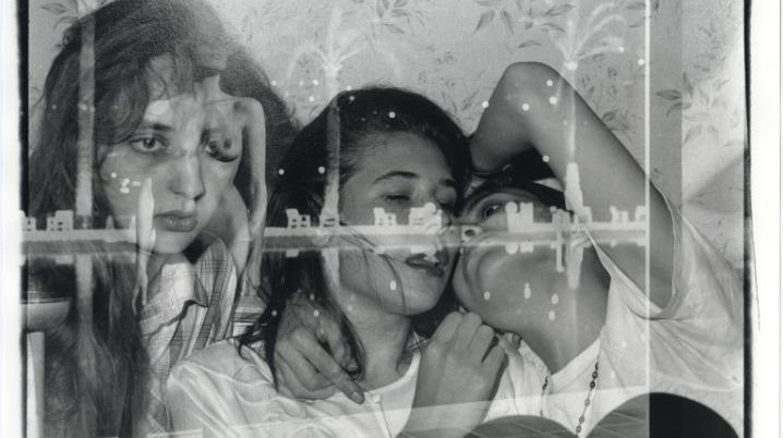 Black-and-white layered photo of three young people in an intimate pose, overlaid with another woman's face and reflections of city lights.
