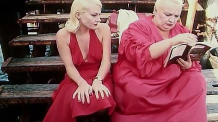 Two actors in red outfits seated side by side and reading a book on the set of Three Stories (1997)