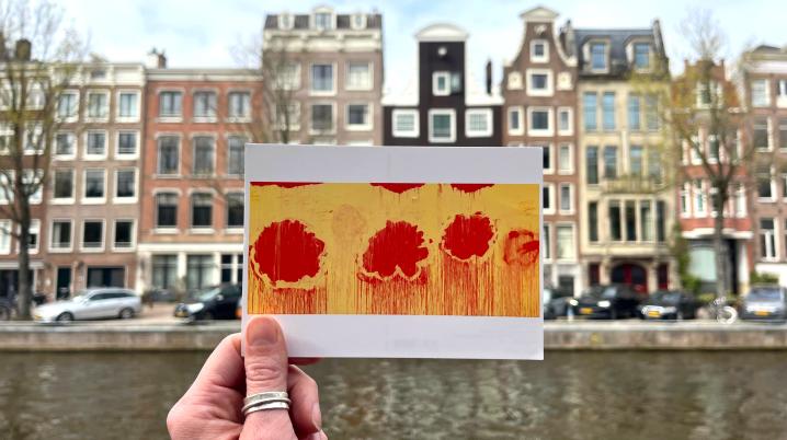 hand holding a postcard with art in front of Amsterdam houses and canal