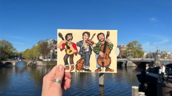 Hand holding postcard with musicians on it in front of Amsterdam canal
