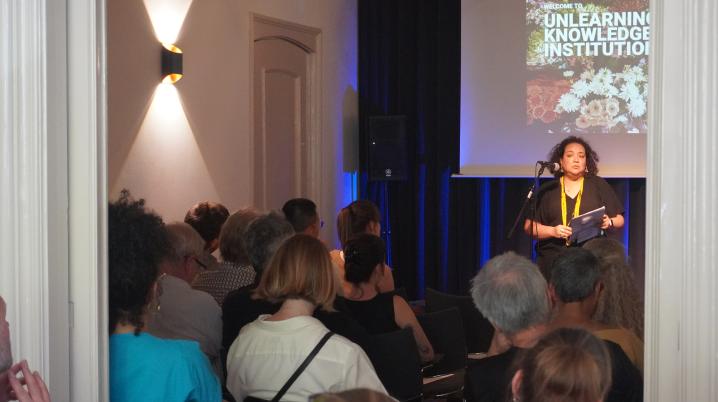 Person behind a mic speaking towards a seated audience
