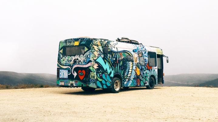 An old school bus covered in colourful paintings riding a desert